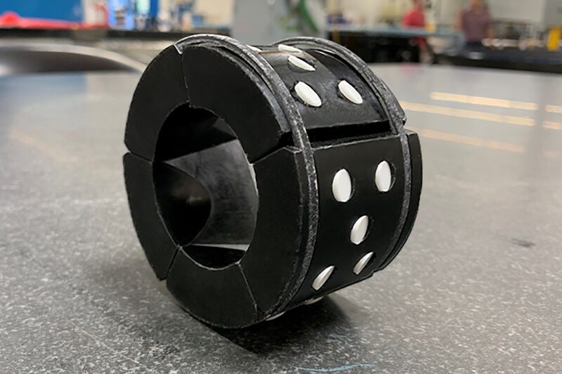 Image of a frac plug composite lower slip, assembled, sitting on a granite surface. It has a short, thick, tubular shape with five forged glass fiber segments held together with two rings.
